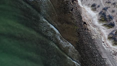 Aerial-top-down-of-calm-ocean-waves-at-rocky-beach-at-day-background