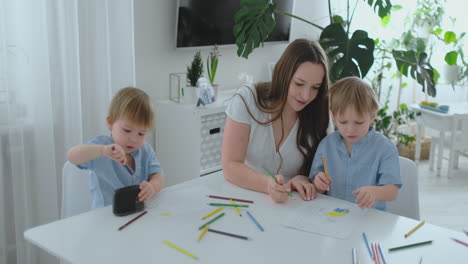 Mom-and-her-two-sons-sitting-at-the-kitchen-table-drawing-colored-pencils-family-drawing-on-the-lawn-in-the-summer.