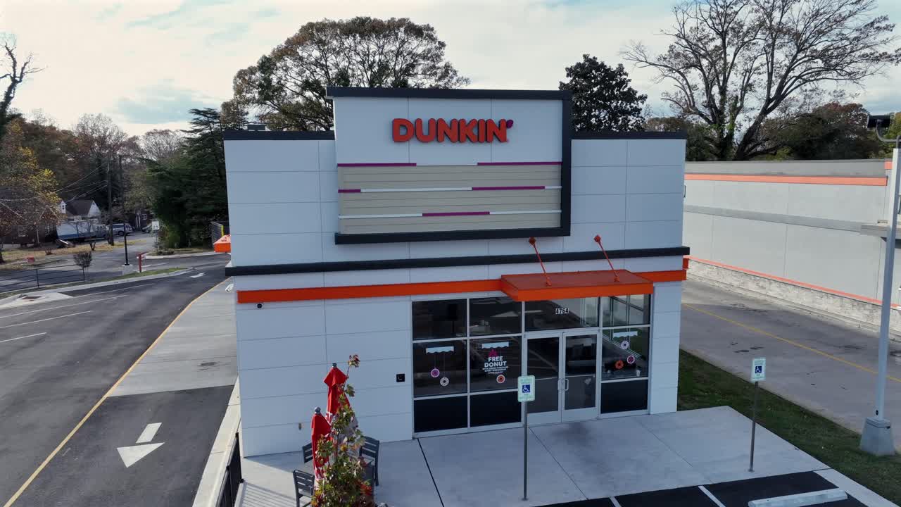 Aerial view of Dunkin’ Donuts Restaurant in american town during autumn season. Decorated christmas tree on terrace. Orbit shot. Colored trees and parking area in backdrop.