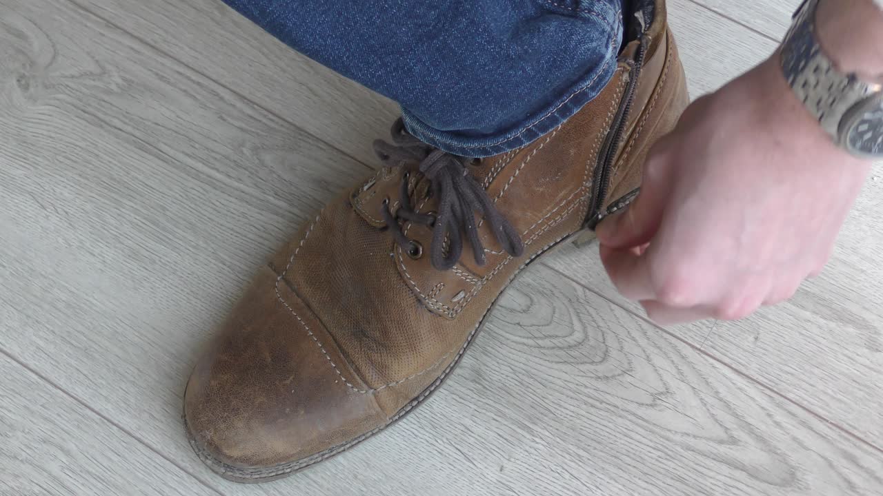Pria melepas sepatu bot setinggi mata kaki di kaki kanannya untuk memperlihatkan kaus kaki warna-warni.