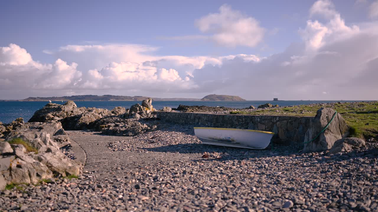 Timelapse of fluffy clouds over Bordeaux Harbour Guernsey on bright day Herm and Jethou in background and small boat on slipway