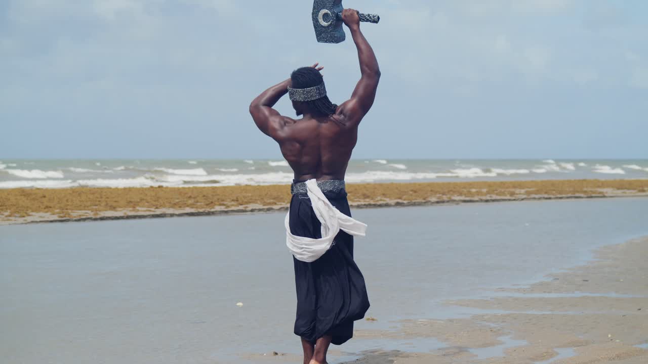 The tropical beach highlights a muscular, dark-skinned man perfectly in character for Nekharis cosplay