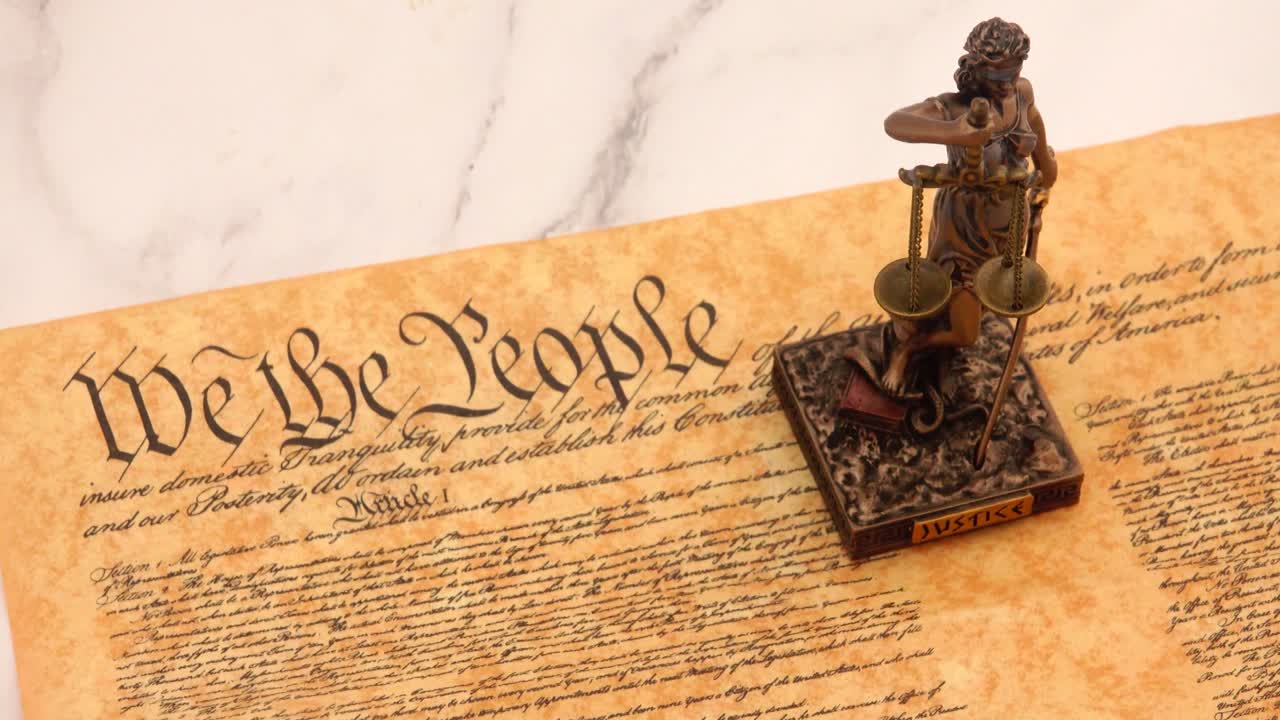 A powerful symbol of law and democracy, the Statue of Justice stands prominently before the United States Constitution, representing fairness, balance, and the rule of law