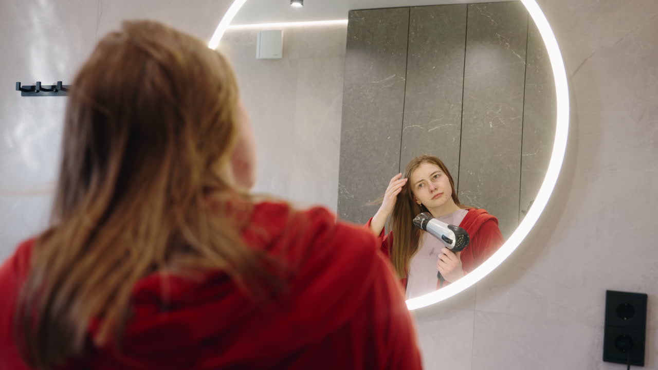 mujer secando su cabello frente a un espejo del baño