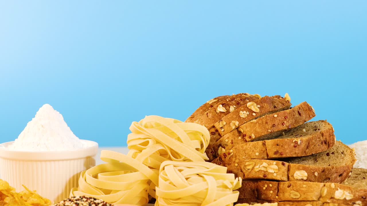 A variety of grains, pasta, and sliced bread arranged on a table with a blue backdrop