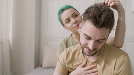 young man sitting on the bed and reading a book while his girlfriend gently caressing him from behind 1