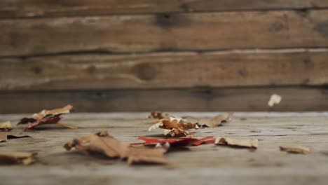 close up view of autumn leaves flying through air against wooden surface