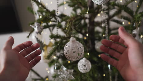 cerca de las manos sosteniendo un ornamento blanco frente a un árbol de navidad decorado