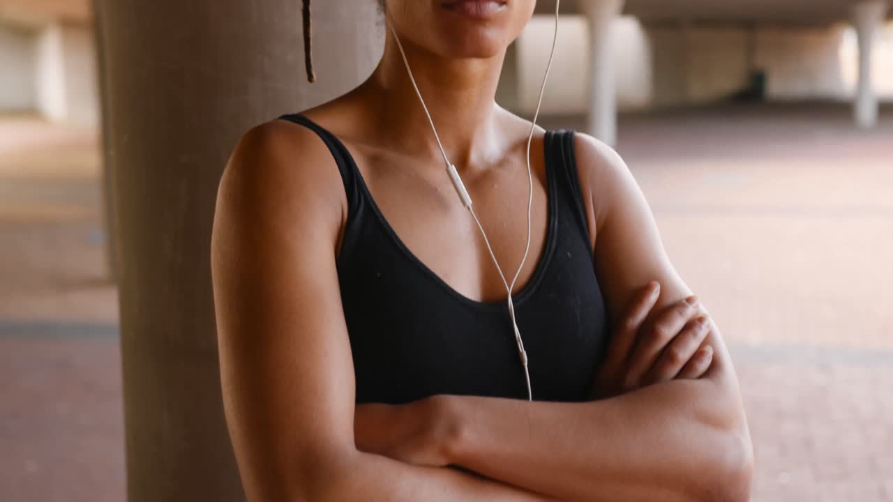 Vista frontale di giovane donna afroamericana che ascolta musica in cuffia in città 4k