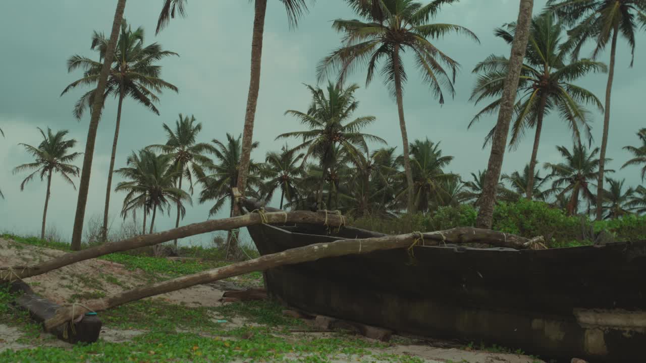 Backward tracking shot of rustic canoe on tropical coast under cloudy sky