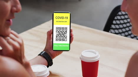 hombre en un café mostrando un teléfono inteligente con certificado de vacunación contra la covid y código qr en la pantalla