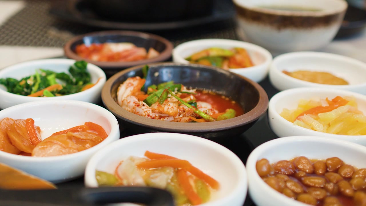 Tangkapan close-up berbagai lauk Korea termasuk kimchi dan acar sayuran di restoran.