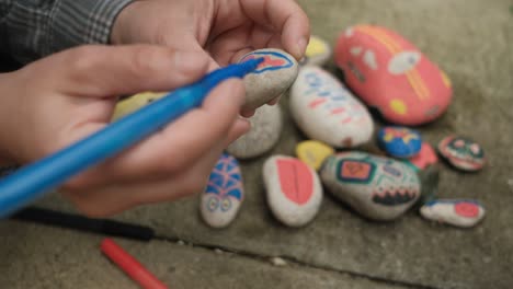 female hands drawing colorful shapes on stones with markers, close up