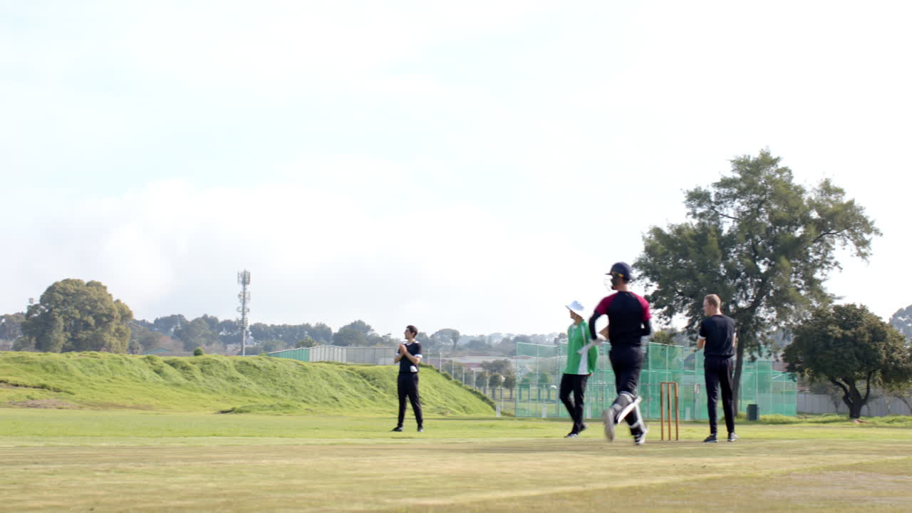 Two teams of multiracial male cricket players and male umpire playing cricket on pitch
