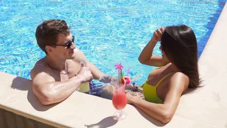 young adult couple flirting and talking in the swimming pool. summertime pool party. slow motion shot