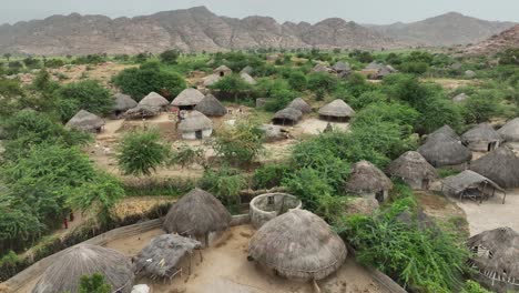 Drone-Aéreo-Girando-Sobre-Cabañas-De-Aldea-En-Nagarparkar,-Sindh,-Pakistán,-Rodeado-Por-Una-Cordillera-En-El-Fondo