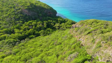 drone flies along ridge line to playa hundu with crystal clear water and current ripples hitting shore