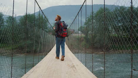 Curious-backpacker-traveling-nature-in-mountains.-Tourist-walk-on-river-bridge.