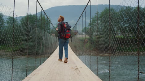 curioso mochilero viajando por la naturaleza en las montañas. paseo turístico en el puente del río.