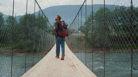 curious backpacker traveling nature in mountains. tourist walk on river bridge.