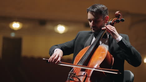 talented cellist in black suit is playing cello on scene of opera house rehearsal of symphonic orchestra