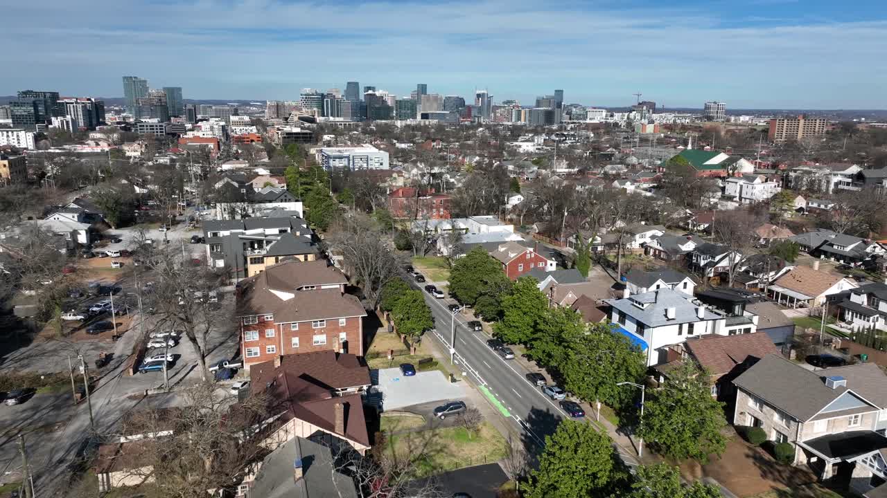 Sorvolo aereo di un quartiere suburbano di Nashville in inverno, con case residenziali e strade alberate che conducono verso lo skyline del centro. Inquadratura ampia. Area residenziale nella zona periferica.