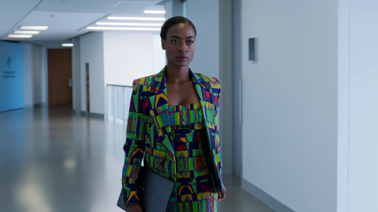 Black Woman Walking Modern Office Corridor Wearing Colorful Patterned Blazer And Skirt, Clutching Leather