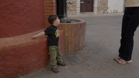 niño niño blanco se apoya en la pared de ladrillo fuente roja, espera a la madre para recogerlo