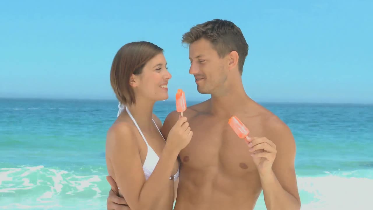 una pareja linda comiendo helados de agua en la playa.