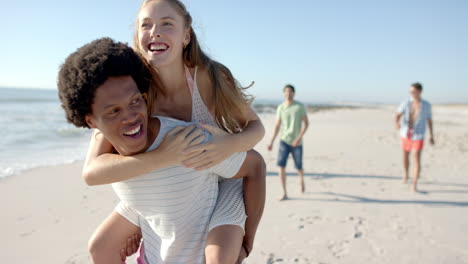 una joven caucásica disfruta de un paseo a espaldas de un hombre afroamericano en la playa.