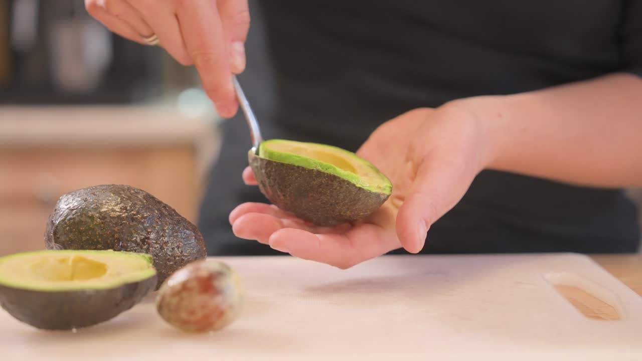 An at-home cook uses a spoon to scoop out half an avocado.