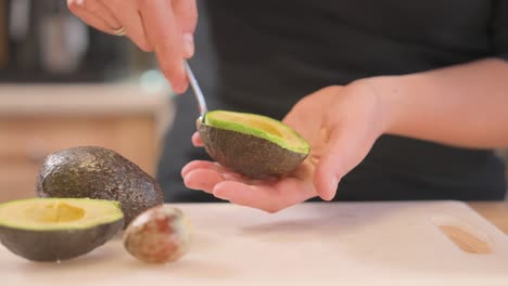 an at-home cook uses a spoon to scoop out half an avocado.