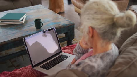 mujer de raza mixta sénior sentada en el sofá usando una computadora portátil