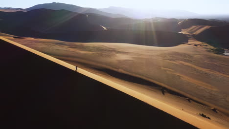 Aerial-view-around-a-man-standing-on-a-dune-in-the-Namib-desert,-in-sunny-Namibia