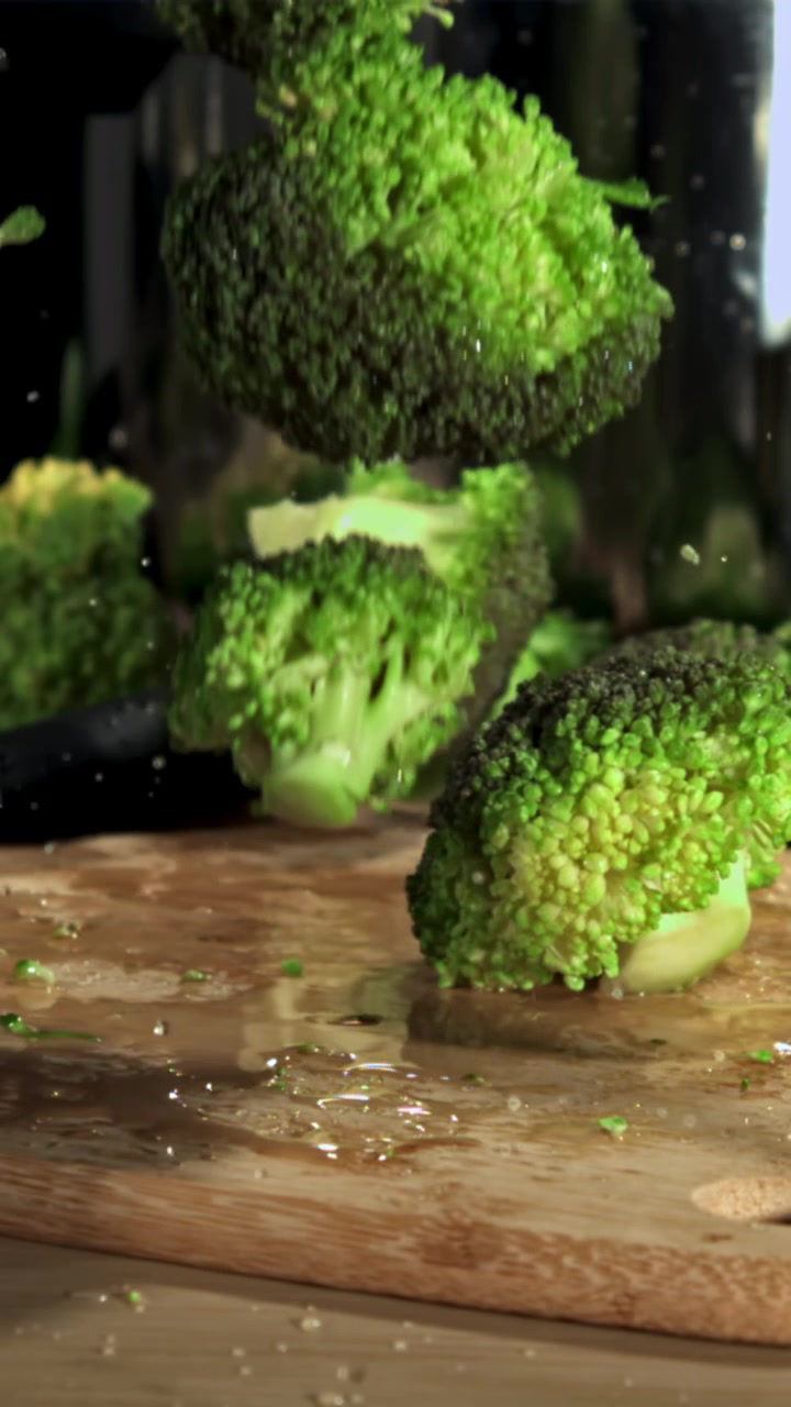 Cimette di broccoli freschi e verdi che cadono su un tagliere bagnato al rallentatore