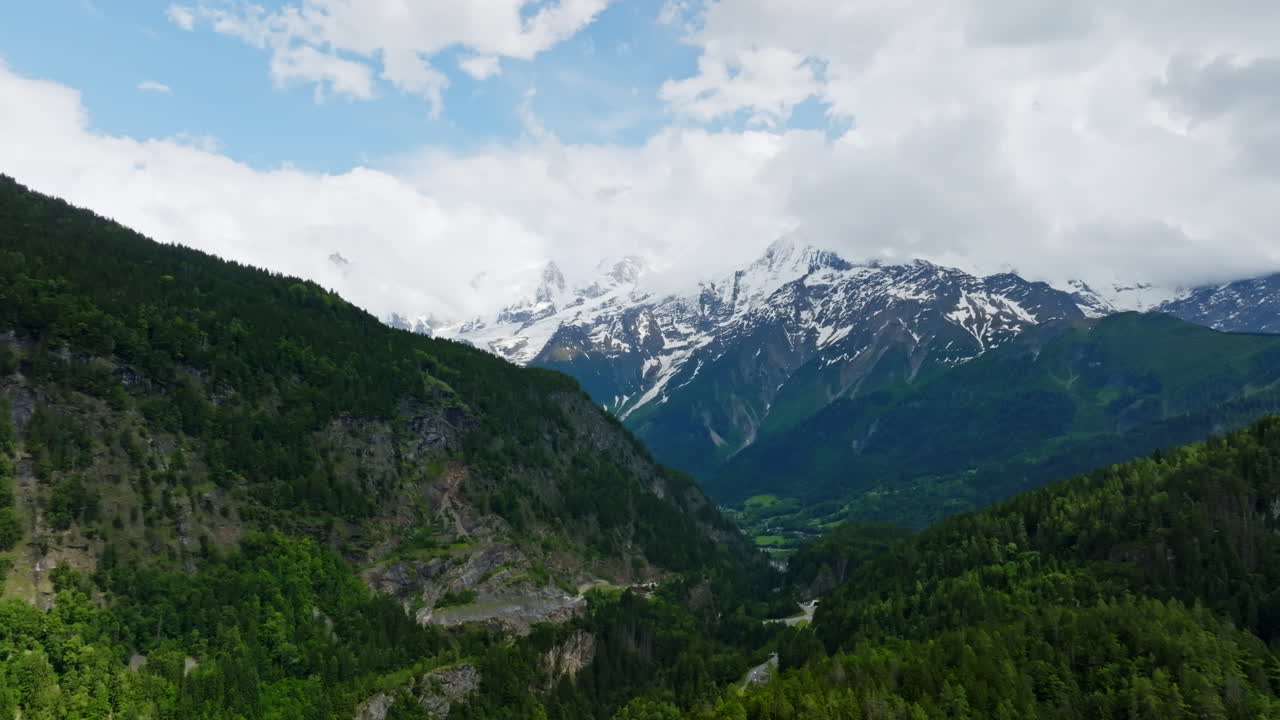 Aerial tracking shot of green and snowy mountain peaks of Hautes-Alpes, France