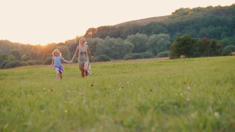 Glückliche-Mutter-Und-Tochter-Rennen-Bei-Sonnenuntergang-über-Das-Feld-Zur-Kamera,-Fröhlicher-Sommer-Und-Vaca