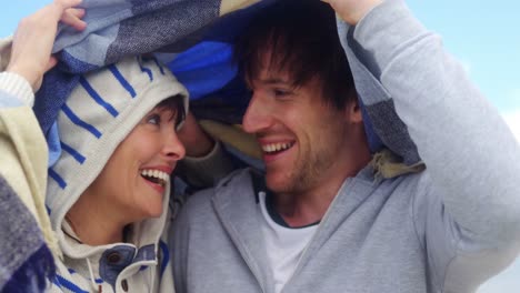 Happy-couple-hiding-in-blanket-at-beach