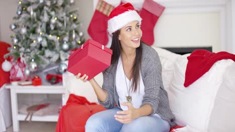 Mujer-Joven-Curiosa-Agitando-Un-Regalo-De-Navidad