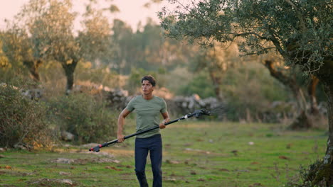 Granjero-Sudoroso-Caminando-Jardín-Naturaleza-Primer-Plano.-Hombre-Sujetando-Rastrillo-Para-Cosechar-Aceitunas