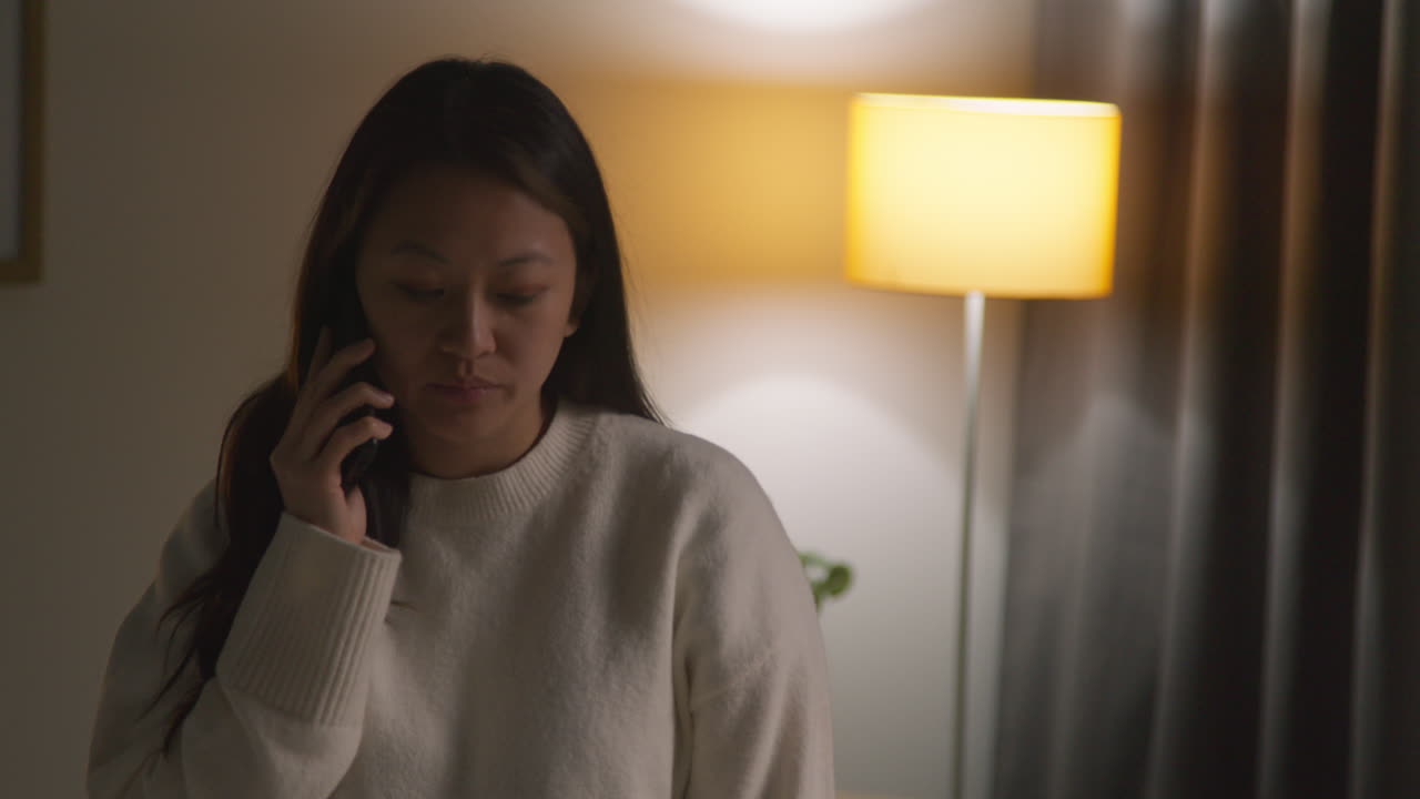 불안하거나 스트레스를 받는 여성이 집에서 저녁을 보내고 라운지를 돌아다니며 드폰으로 이야기하고 있습니다.