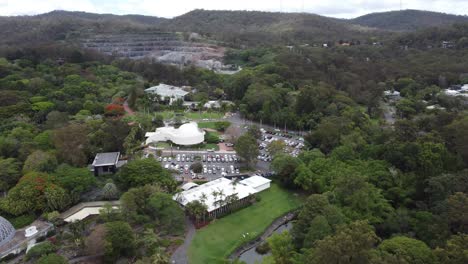 Drone-flying-towards-a-Planetarium-over-gardens-and-carpark