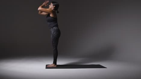 studio shot of mature woman wearing gym fitness clothing standing on mat doing variety of pilates stretching exercises