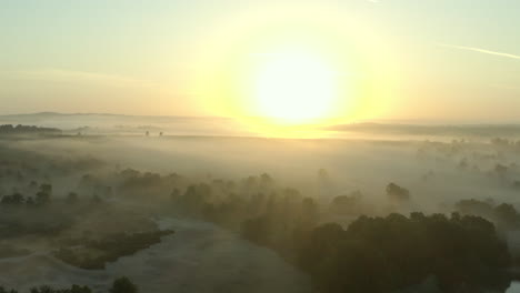 a misty, foggy sunrise in the beautiful english countryside, with trees and a lake in the foreground