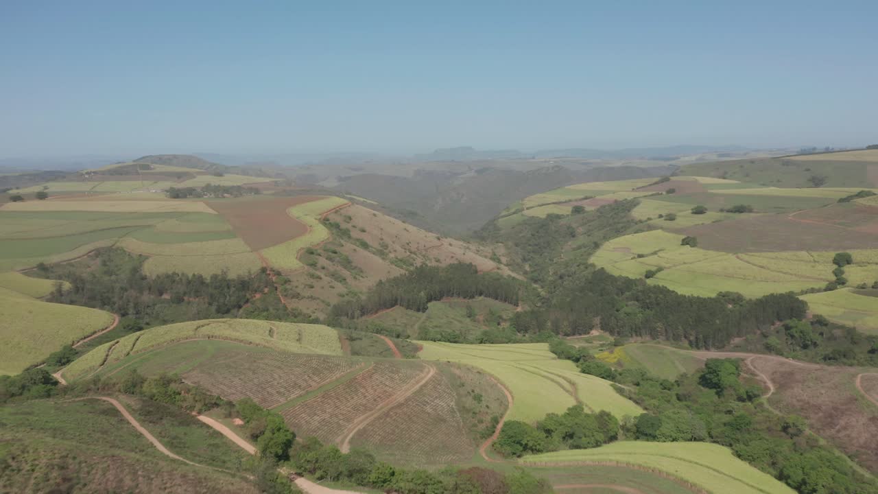 Aerial view moving over dense valley forest, crop fields and green hilly countryside
