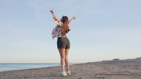 Wide-shot-young-happy-woman-smiling-and-spinning-on-the-beach-with-her-arms-in-the-air