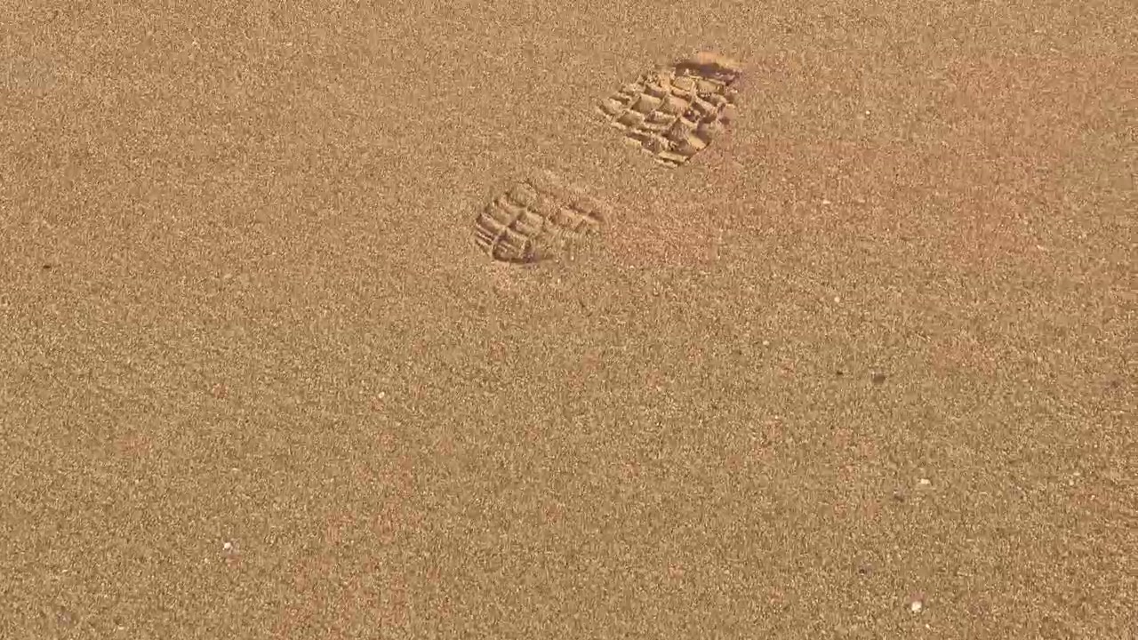 Caminhar e seguir pegadas distintas impressas na areia, destacando o caminho de alguém que caminhou recentemente pela costa