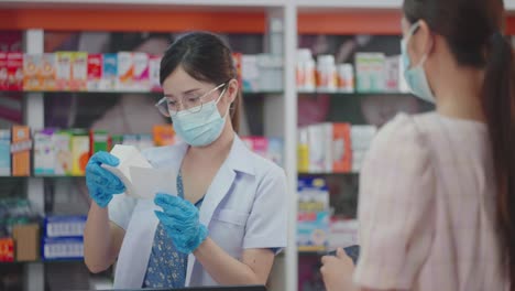 asian female pharmacist wearing a protective hygienic mask and glove selling prescription medicine to customers.