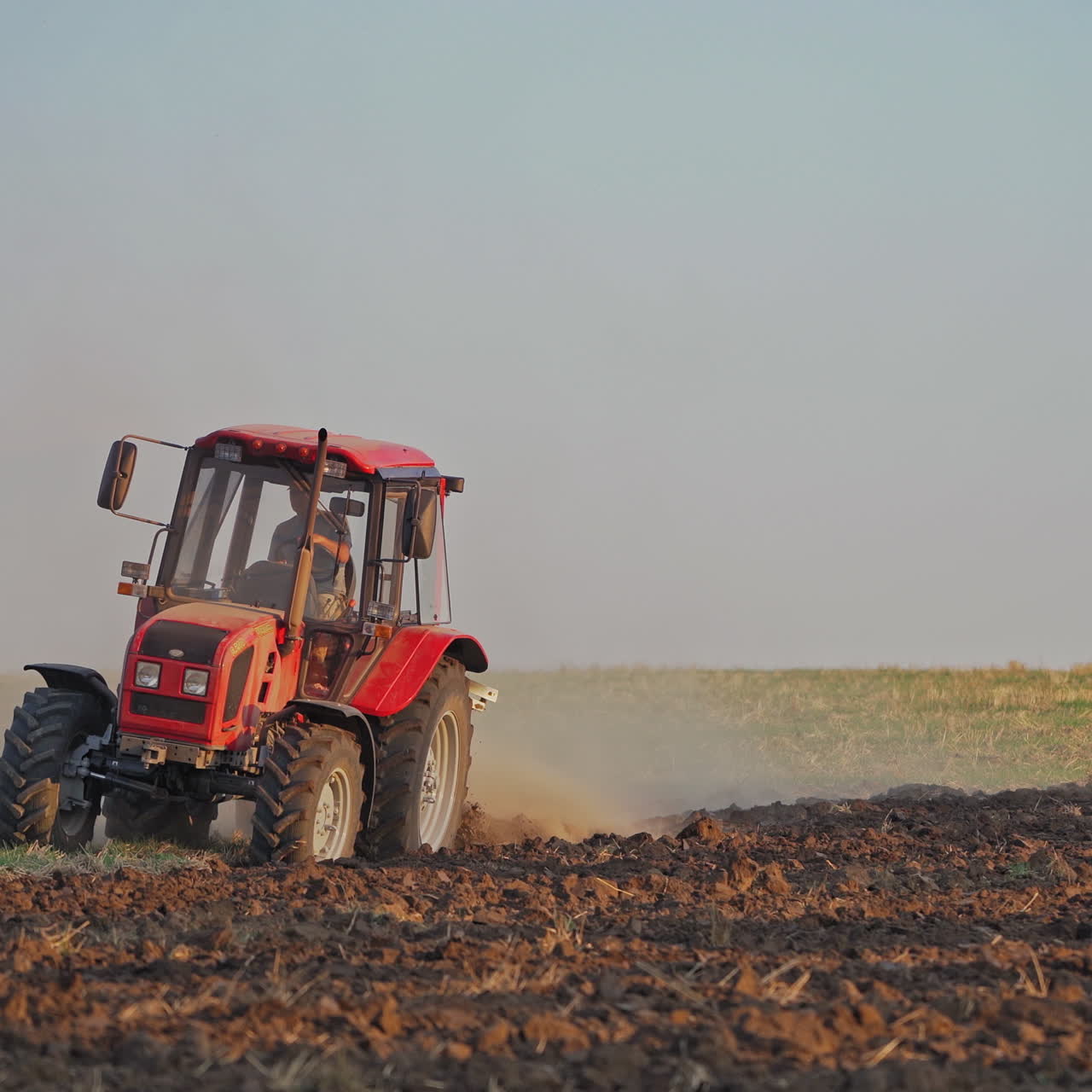 Red tractor at work. Agricultural machine plowing the field at daytime. Cultivation of land outdoors.