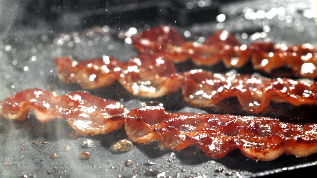 Strisce di pancetta che sfrigolano e friggono in una padella calda